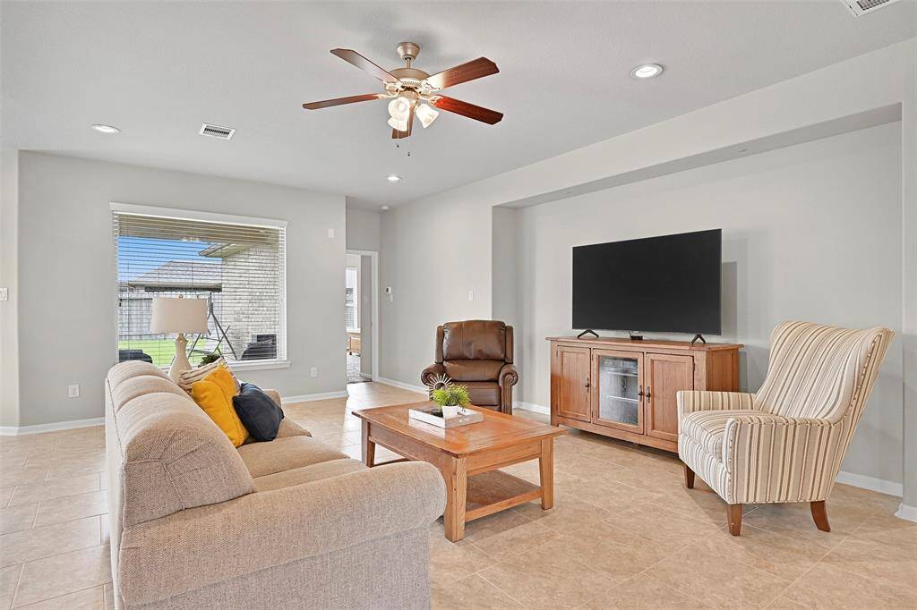 The spacious living room features neutral tile flooring, recessed lighting, and a ceiling fan, with a large window providing views of the backyard and allowing natural light to fill the space. A recessed wall niche offers a perfect spot for media storage or decor.