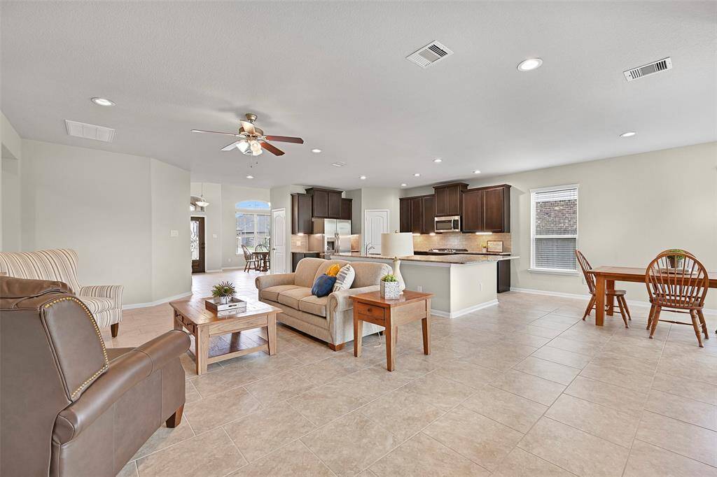 This open-concept floorplan seamlessly connects the living room, kitchen, and casual dining space—perfect for entertaining. The neutral tile flooring continues throughout, complementing the dark wood cabinetry and granite counters in the kitchen, while recessed lighting brightens every corner.