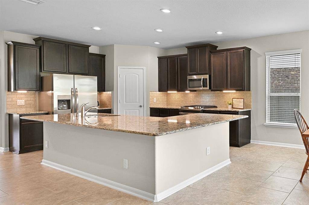 The open-concept kitchen features rich espresso cabinetry, granite countertops, a subway tile backsplash, and a massive island with breakfast bar seating—perfect for entertaining or everyday living.