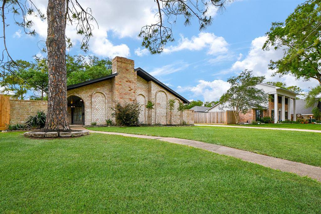 Charming single-story brick home with unique arched windows and a well-maintained lawn. The property features mature trees and a paved walkway, creating a welcoming curb appeal.