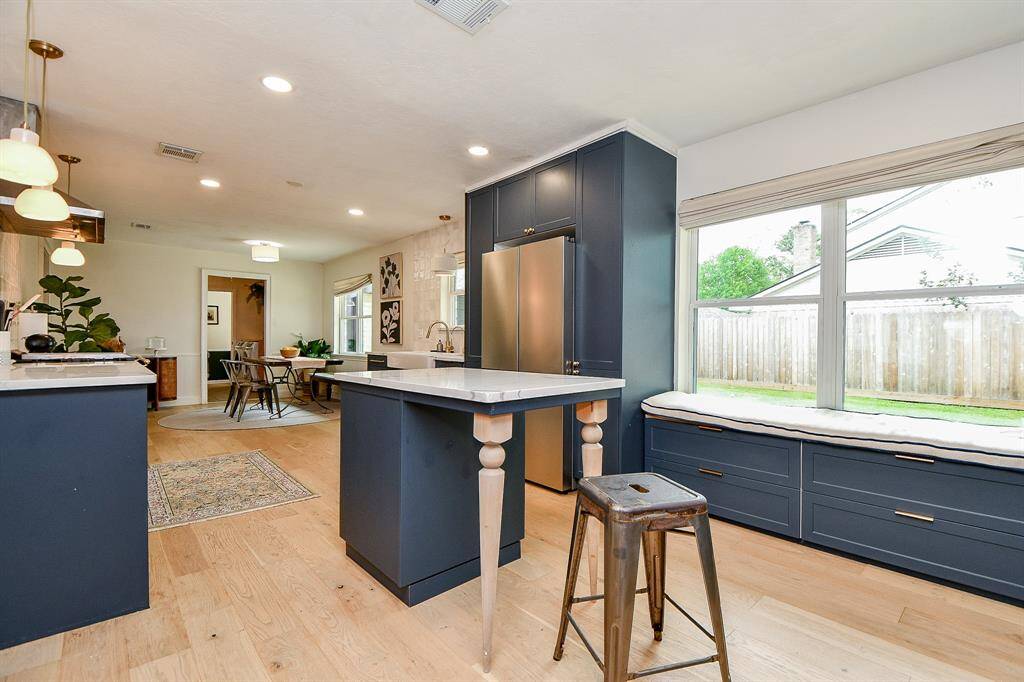This spacious kitchen features modern navy cabinetry, a central island with seating, and large windows for natural light. It opens into a cozy dining area, perfect for entertaining.