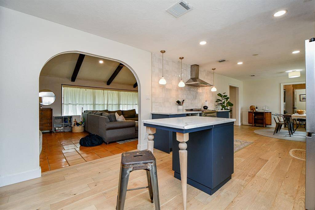 This open-concept home features a modern kitchen with an island, stylish pendant lighting, and a cozy living area with exposed beams. The space is bright with wood and tile flooring, creating a warm and inviting atmosphere.