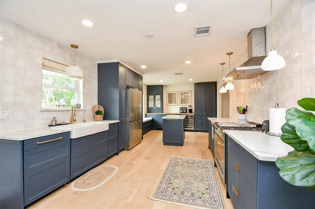 Bright, modern kitchen with navy cabinets, stainless steel appliances, and light wood flooring. Features a farmhouse sink, ample counter space, and stylish pendant lighting.