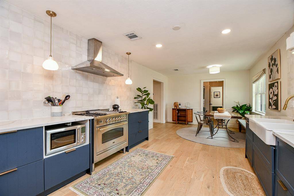 This spacious kitchen features modern blue cabinetry, a stainless steel range, and a farmhouse sink. It has light wood flooring, stylish pendant lights, and a cozy dining area with natural light. Perfect for cooking and entertaining.