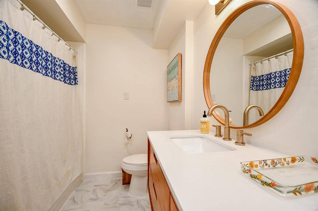 This bathroom features a modern design with a large circular mirror, elegant brass fixtures, and a stylish vanity. The shower curtain adds a pop of color with its blue pattern, complementing the neutral tones of the room.