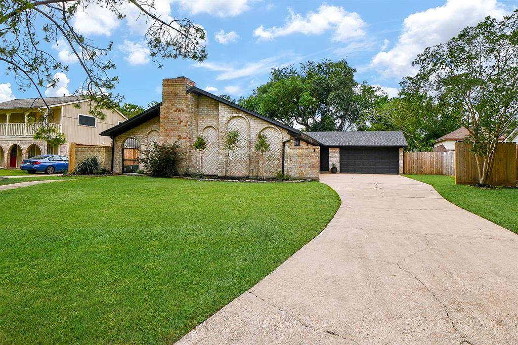 This photo showcases a charming single-story brick home with a modern, dark garage door. The property features a spacious driveway, well-maintained lawn, and mature trees, offering a welcoming curb appeal in a suburban neighborhood.