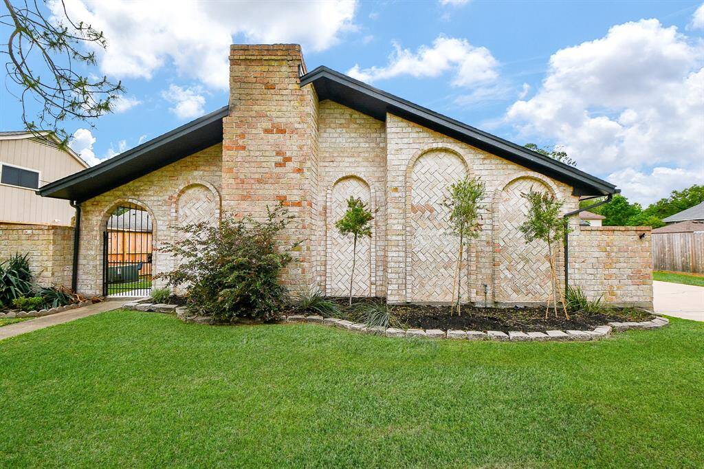 This charming home features a unique brick exterior with arched accents and a prominent chimney. A well-maintained lawn and tasteful landscaping enhance its curb appeal, while a gated entrance adds a touch of elegance and security.