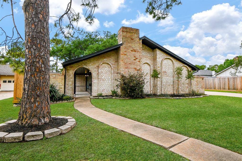 This charming brick home features a sloped roof and a welcoming arched entryway. The well-maintained front yard is landscaped with trees and shrubs, offering great curb appeal.