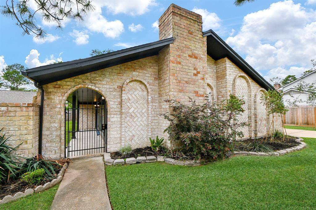 Charming brick home with arched entryway and landscaped front yard. Features a gated walkway and lush greenery, providing a welcoming and secure atmosphere.