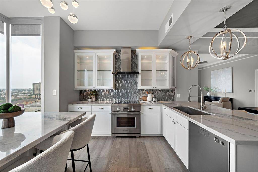 Everyday cooking is elevated in a layout that centers around a gleaming cooktop and vent hood, framed by vertical tilework and airy glass-front storage.
