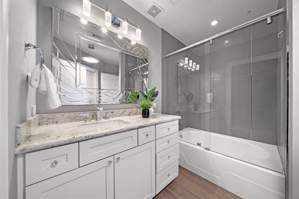 Adjacent to the bedroom, the secondary bath features a marble-topped vanity with ample storage and a full shower/tub combination enclosed in sleek sliding glass.