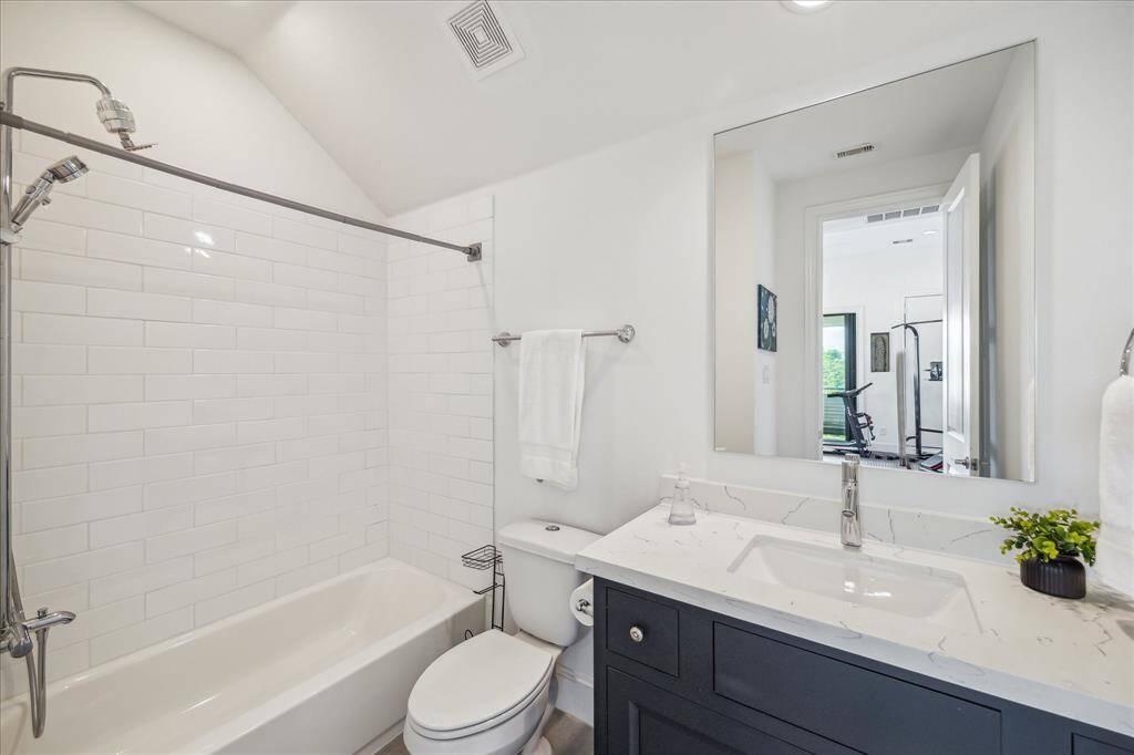 The ensuite bath features a clean and modern design with white subway tile, a sleek quartz-topped vanity, and a soaking tub/shower combo.