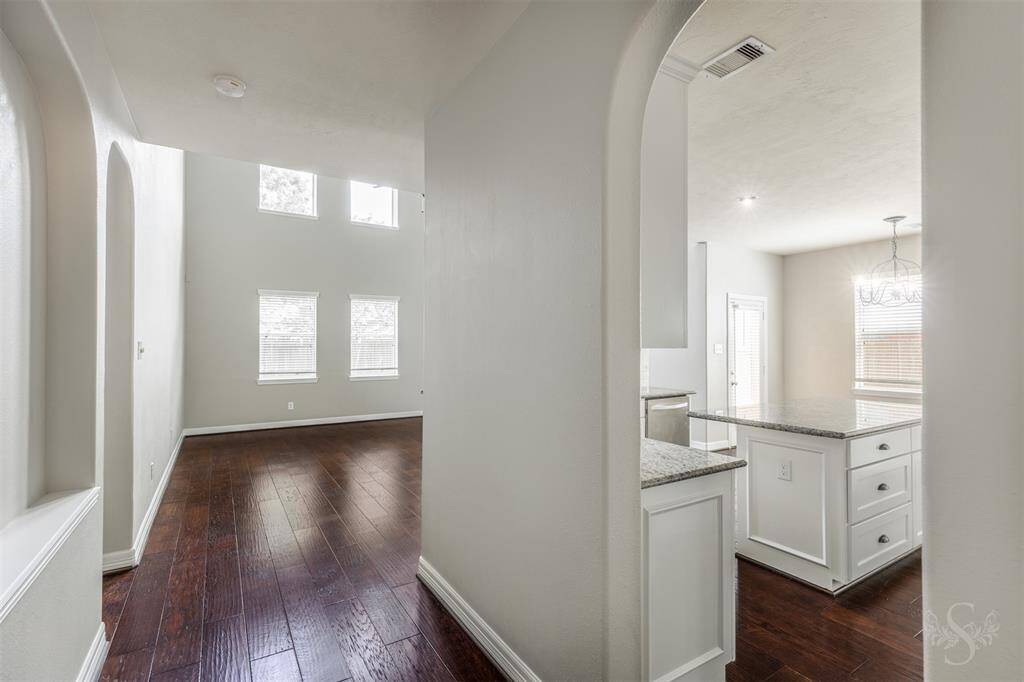 As you stand in the hallway, a captivating vista unfolds before you, showcasing the harmonious blend of design and function in this home. To your right, the kitchen invites you in with its sleek, modern appeal. The custom-built white wood cabinets and gleaming granite countertops create a stunning contrast against the warm, hickory wood floors that stretch throughout the space.