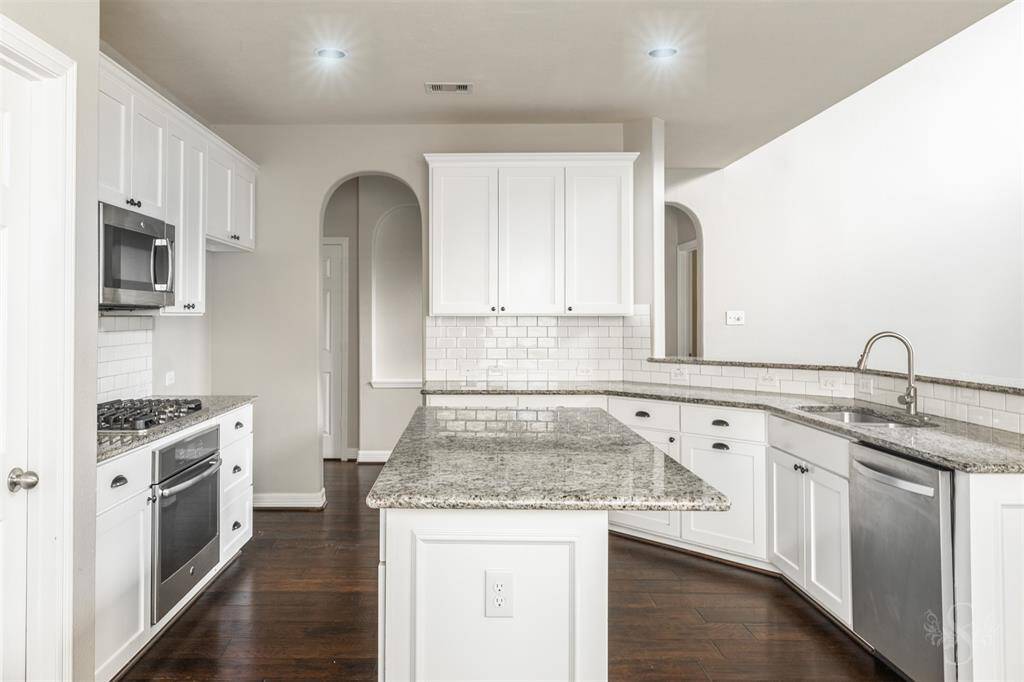 The kitchen is a masterpiece of modern design and functionality, featuring an elegant combination of white cabinets, granite countertops, and rich wood floors. The custom-built white cabinets provide ample storage while maintaining a sleek and clean aesthetic, their simplicity and elegance enhanced by stylish bronze hardware.