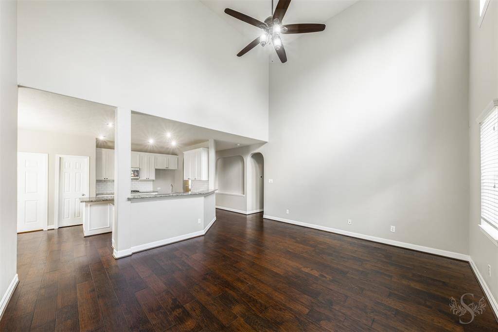 As you stand in the living room, your gaze effortlessly transitions into the heart of the home—the kitchen. The rich hue of the wood floors binds these spaces together, creating a seamless and inviting flow. Sunlight streams through large windows, enhancing the warm tones of the floors and illuminating the open-concept design.