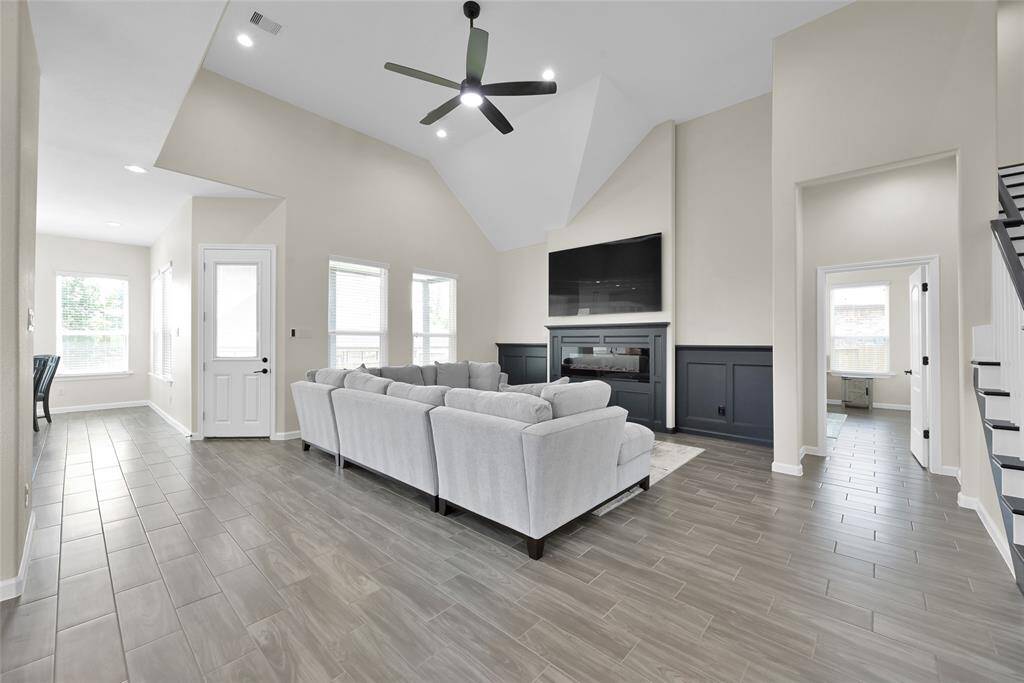 Living room boasts high ceilings, abundant natural light, and a sleek electric fireplace, perfect for both relaxing and entertaining.