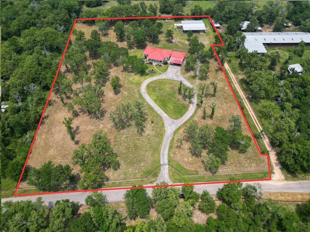 Expansive rural property with a long winding driveway leading to the farmhouse. Surrounded by open fields and mature trees, offering privacy and space. Additional outbuildings and ample greenery enhance the scenic, secluded setting.