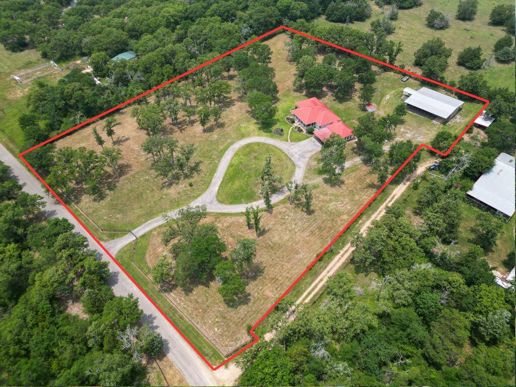 This photo showcases a charming country home with a red roof, surrounded by lush greenery. The property features a long, winding driveway and a spacious front & side yards.