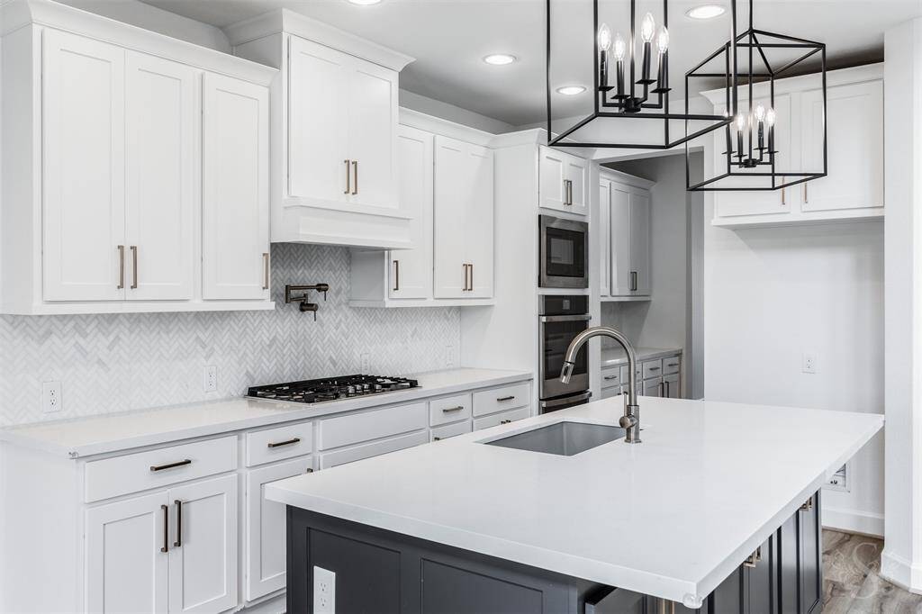 Under stylish geometric pendant lights, the oversized quartz island anchors the heart of the home, offering ample prep space and seating. This culinary space also showcases custom white cabinetry, gas cooktop with pot filler and spectacular herringbone tile backsplash. The sophisticated hardware and clean lines create a fresh, refined aesthetic.