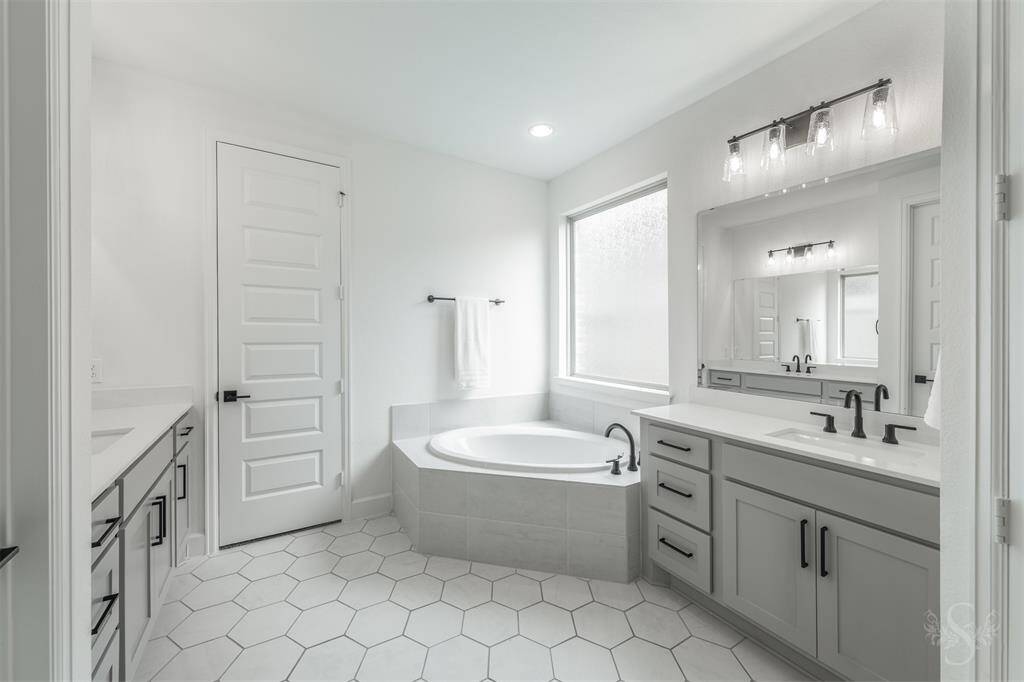 Indulge in the spa-inspired primary bath, complete with a soaking tub beneath a frosted window, dual vanities with quart countertops, and designer lighting. The crisp white palette and oversized hexagon tile flooring add a touch of modern luxury.