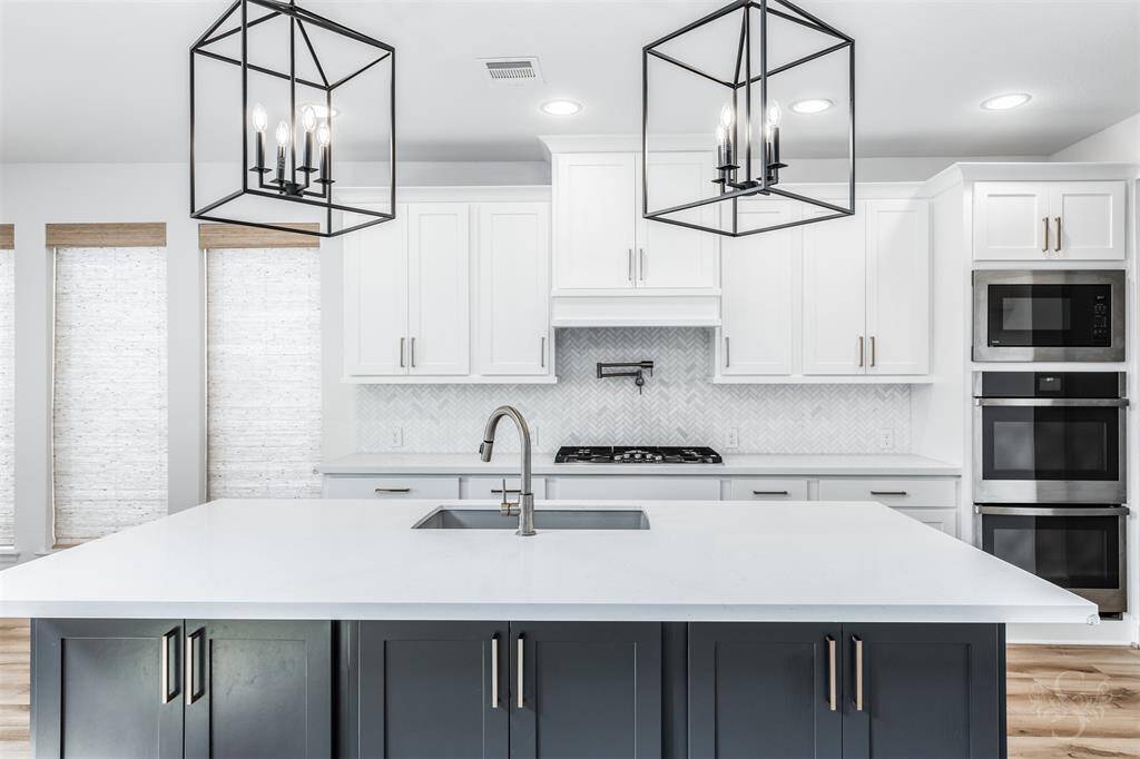 A chef’s dream kitchen featuring a striking quartz island with undermount sink, designer pendant lighting, contrasting cabinetry for a modern touch, gas cooktop, pot filler and stainless steel appliances including double ovens! Crisp white cabinets and a herringbone tile backsplash elevate the space with timeless elegance.