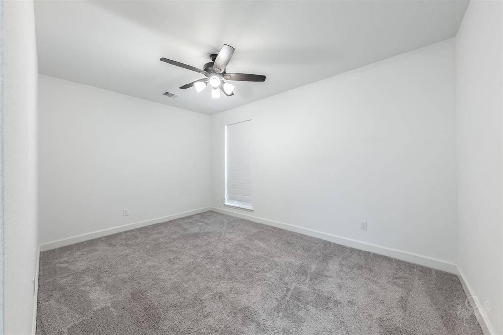 Perfect for multigenerational living or guests, this first-floor secondary bedroom offers comfort and privacy with plush carpet and neutral tones. A ceiling fan and nearby full bath make it an ideal retreat for long-term stays or weekend visitors.