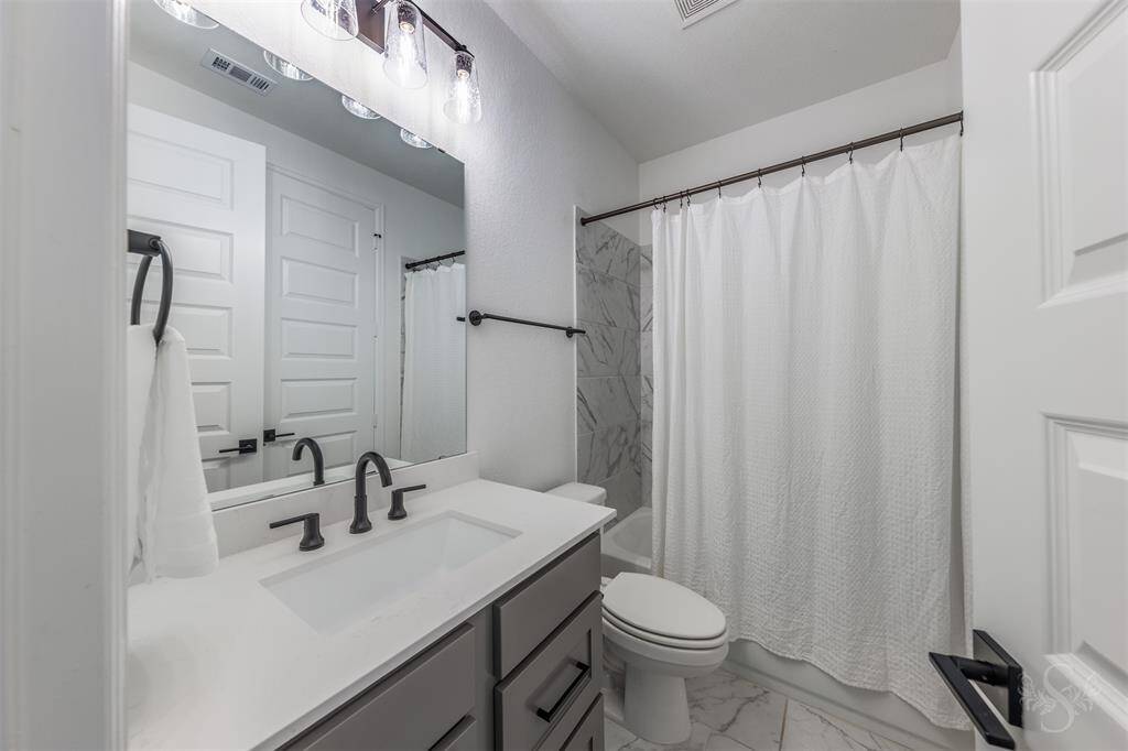 This elegant full bath features a sleek vanity with quartz countertops, matte black fixtures, and a tiled shower/tub combo with a marble-style surround. A perfect blend of style and function, just steps from the in-law suite.