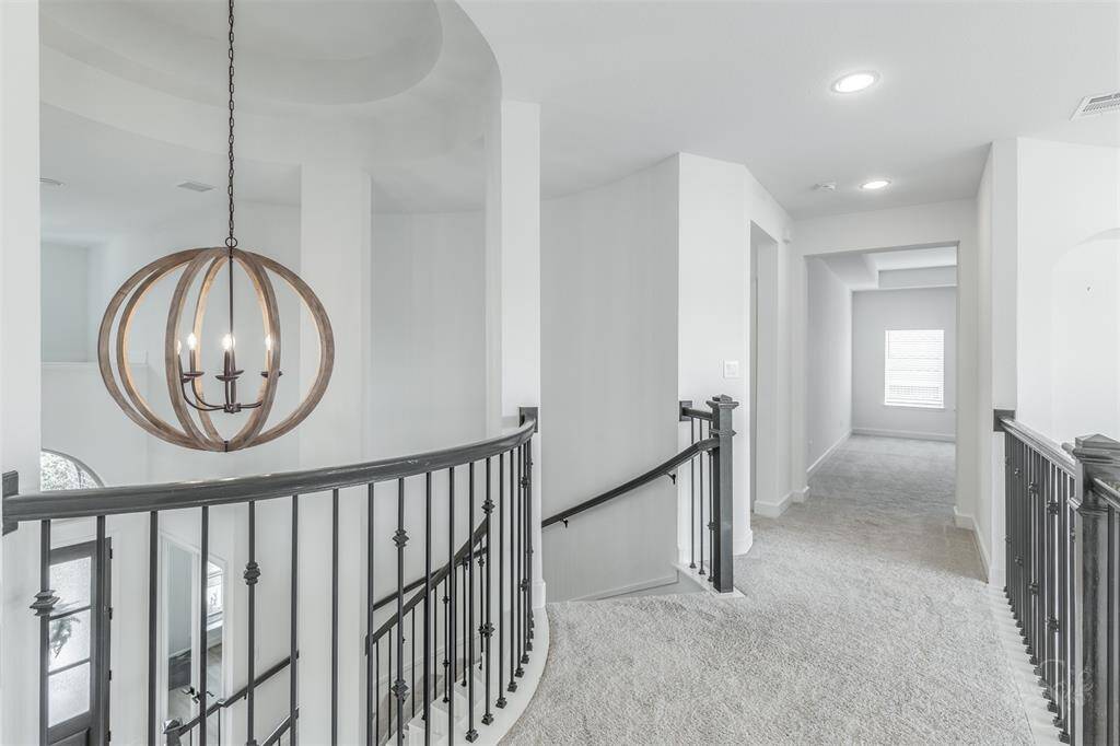 The curved staircase leads to an airy upstairs landing with plush carpeting and wrought-iron spindles. A dramatic designer chandelier adds architectural interest and connects the levels with elegance.