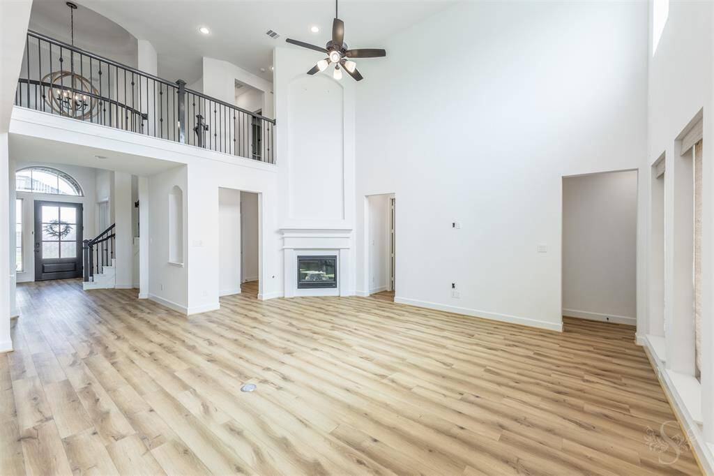Soaring ceilings and a dramatic wall of windows bathe the family room in natural light, complemented by a gas fireplace and elegant balcony overlook. The open layout enhances both daily living and upscale entertaining.