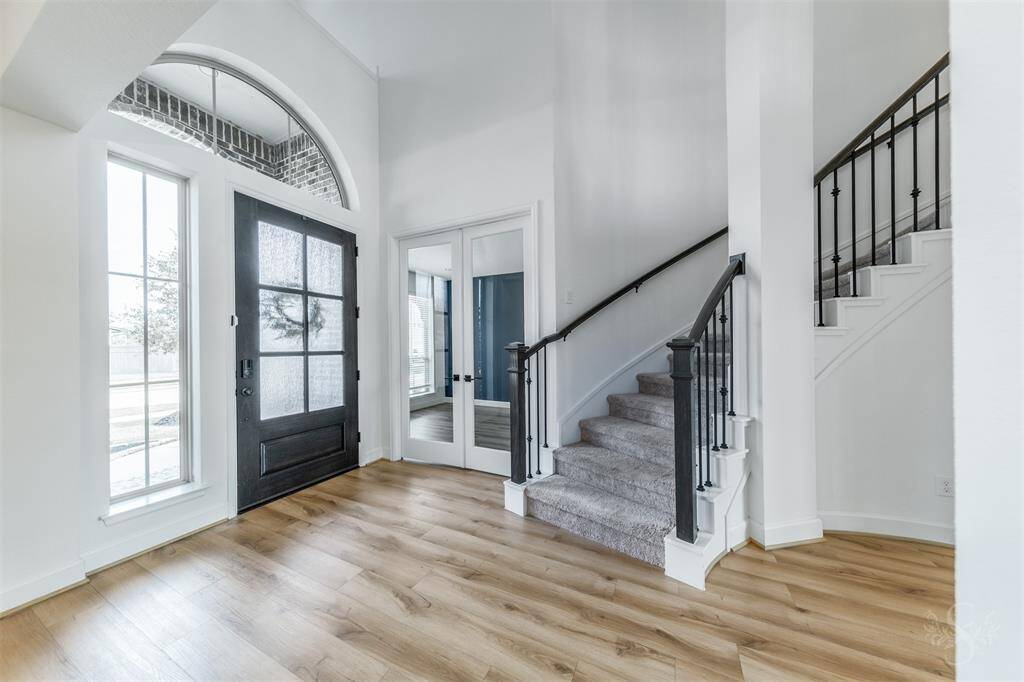 Step into a grand foyer with soaring ceilings, gorgeous flooring, and a sweeping staircase accented by wrought iron spindles. Double glass doors lead to a private study, perfect for work or quiet retreat.