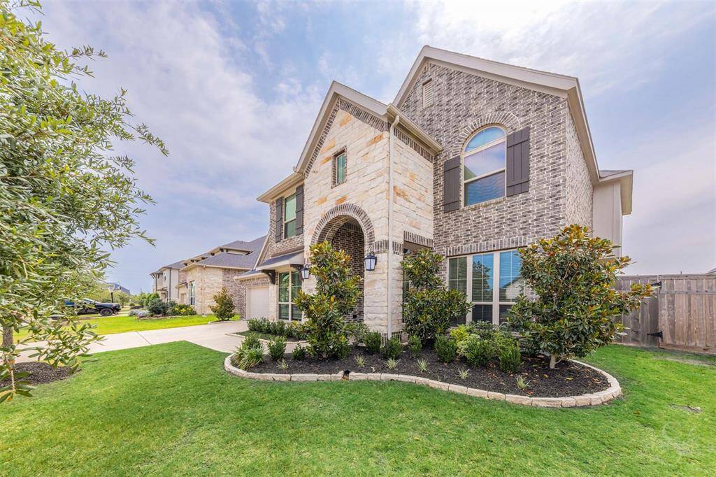 Lush landscaping and manicured garden beds complement the beautiful architectural details, creating a warm and inviting front elevation.