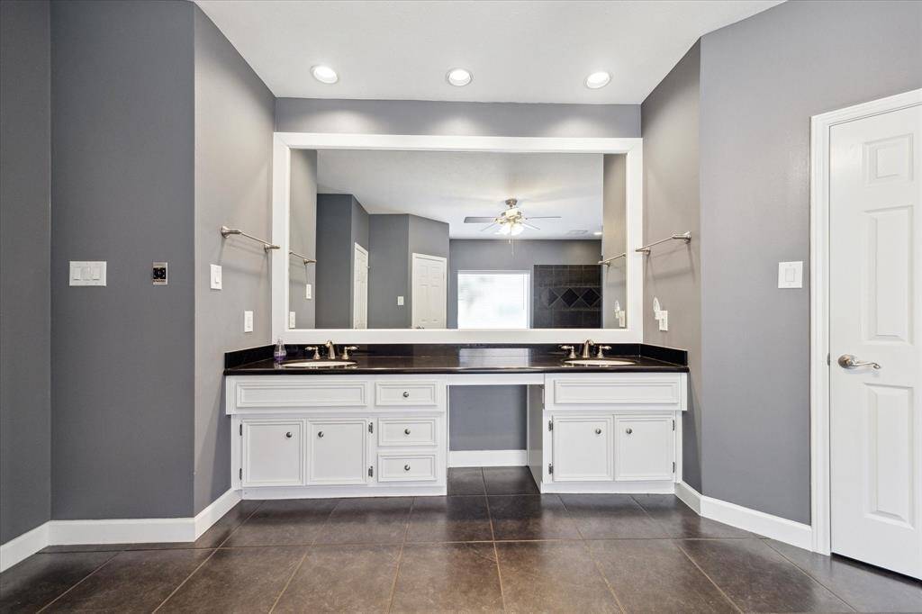 This modern bathroom features a sleek dual-sink vanity with white cabinetry and black countertops. The large mirror and recessed lighting enhance the spacious feel, while the gray walls and tile flooring add a contemporary touch.