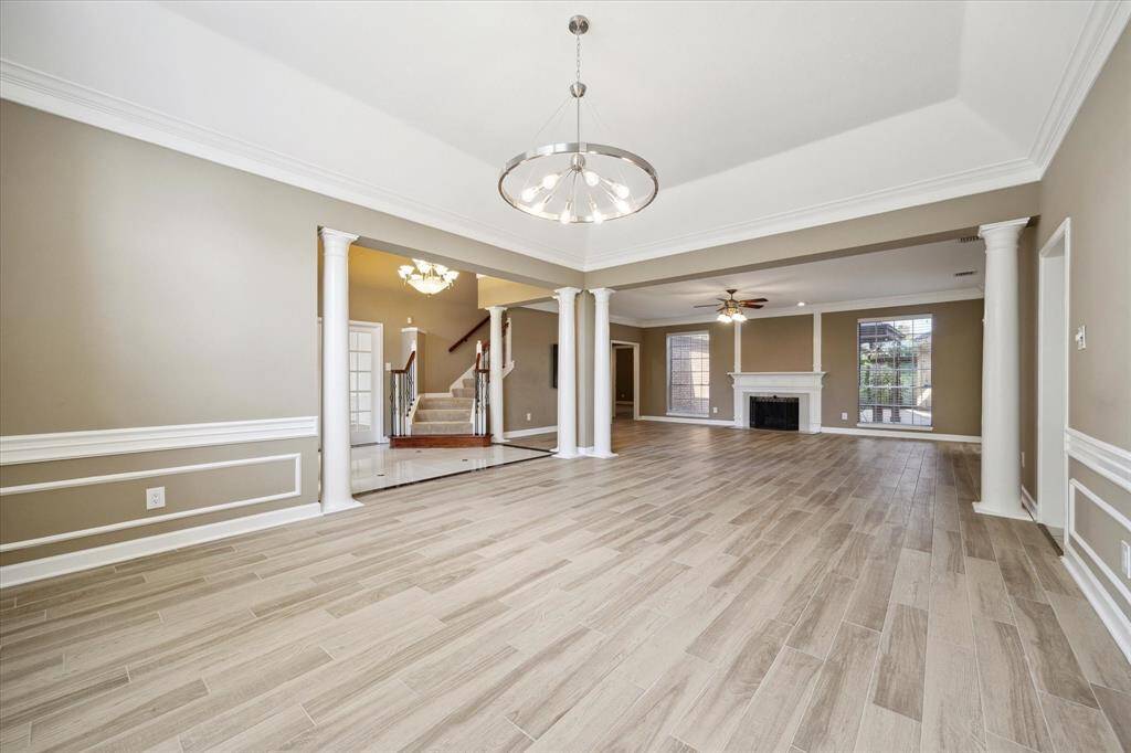 This spacious open-concept living area features elegant flooring, neutral walls, and decorative white trim. It includes a contemporary chandelier, a cozy fireplace, and large windows for natural light.