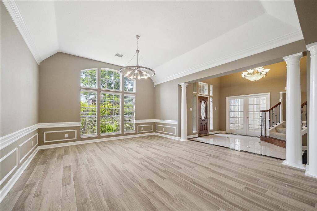 This elegant living space features high ceilings, large arched windows for natural light, and stylish, durable porcelain flooring. The room is accentuated by classic wainscoting and contemporary lighting, leading to a grand entrance with columns and lovely staircase.