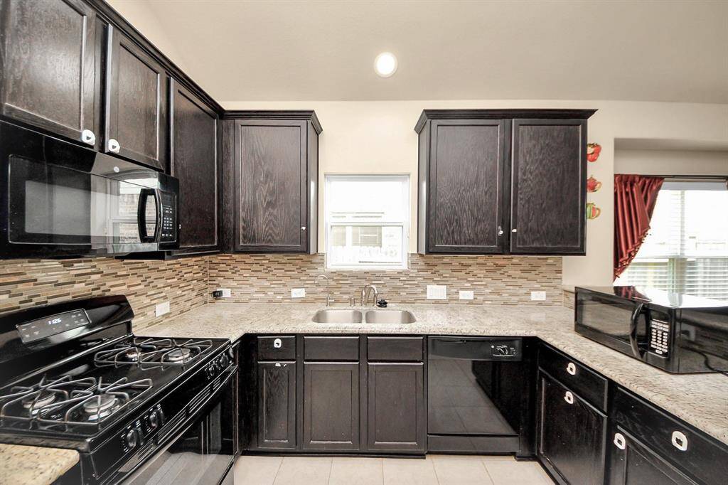 Modern kitchen with dark wood cabinets, granite countertops, and a mosaic tile backsplash. Equipped with a gas stove, microwave, and plenty of storage, it offers a sleek and functional cooking space.