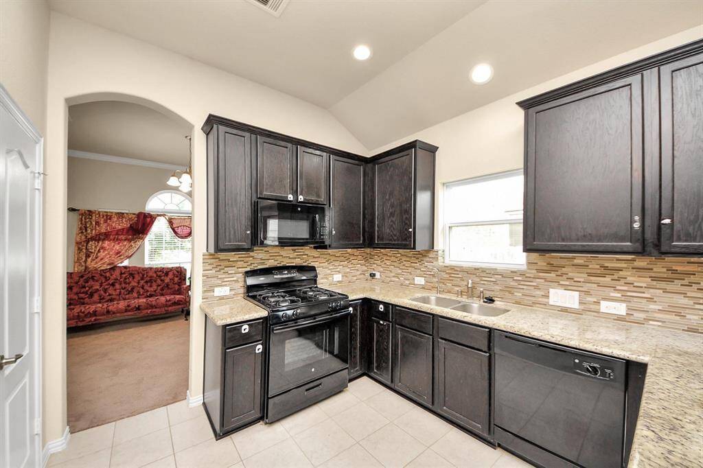 It flows into an open kitchen with dark cabinetry and light countertops. Cozy red seating adds warmth, and recessed lighting enhances the bright, inviting atmosphere.