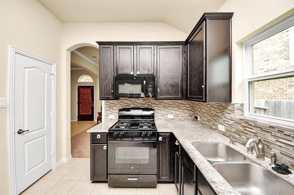 This kitchen features dark wood cabinets, a gas stove, and a modern tile backsplash. It includes stainless steel appliances, a double sink, and plenty of natural light from the window.