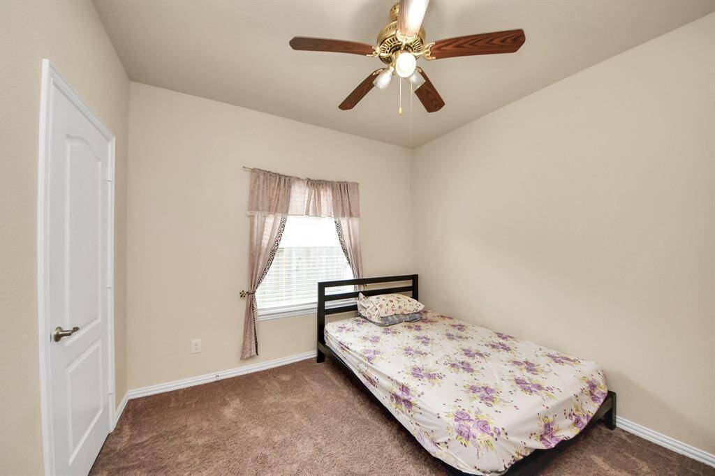 Cozy secondary bedroom with neutral walls and carpet, featuring a ceiling fan, single bed, and a small desk by a window with natural light.