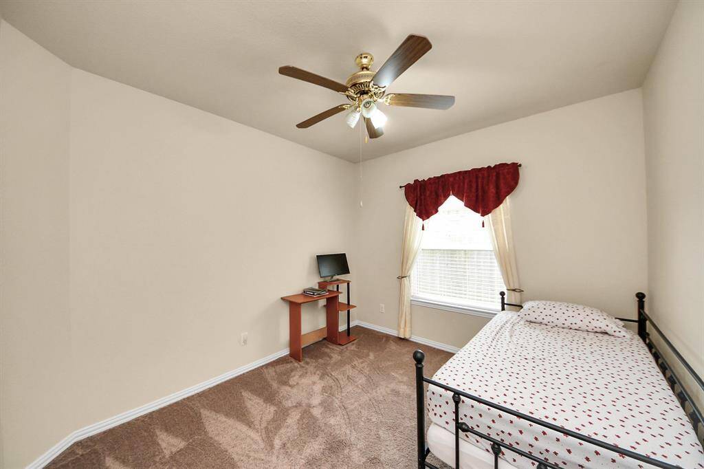 Cozy 3rd bedroom with neutral walls and carpet, featuring a window with soft curtains, a ceiling fan, and a single bed with floral bedding. Ideal for a guest room or small bedroom.
