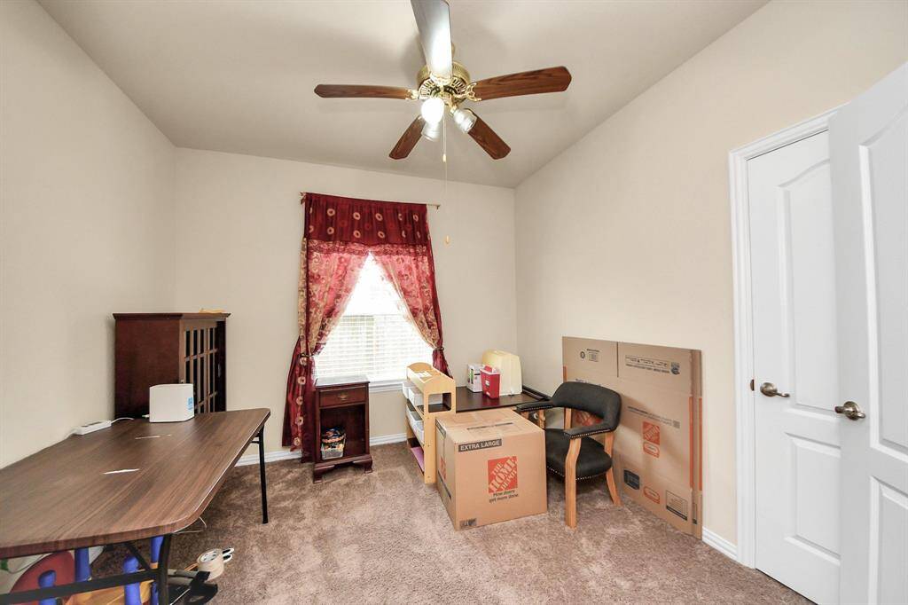 Spacious loft area/4th bedroom with neutral walls and carpet, featuring red-accented furniture and drapery. Large windows allow natural light, and there's a ceiling fan for comfort.