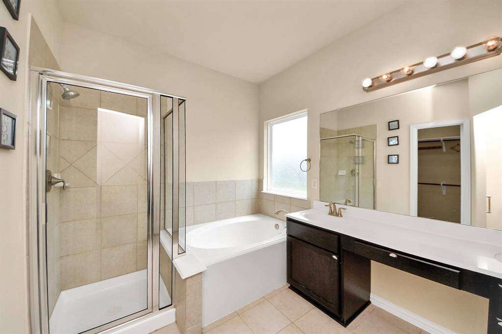 Bright and spacious bathroom featuring a glass-enclosed shower, a separate bathtub, a large mirror, and a modern vanity with ample storage.