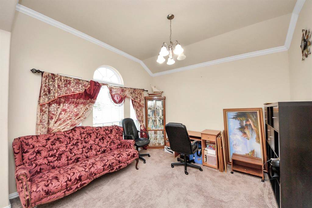 This cozy room includes a decorative couch, an office chair at a small desk, a glass display cabinet, and vibrant drapes over a window, offering a versatile space for relaxation or work.