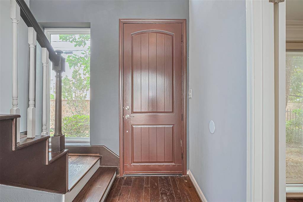 Inviting entryway featuring a wooden front door, adjacent to a staircase with white railings. A large window beside the stairs offers natural light and a view of greenery.