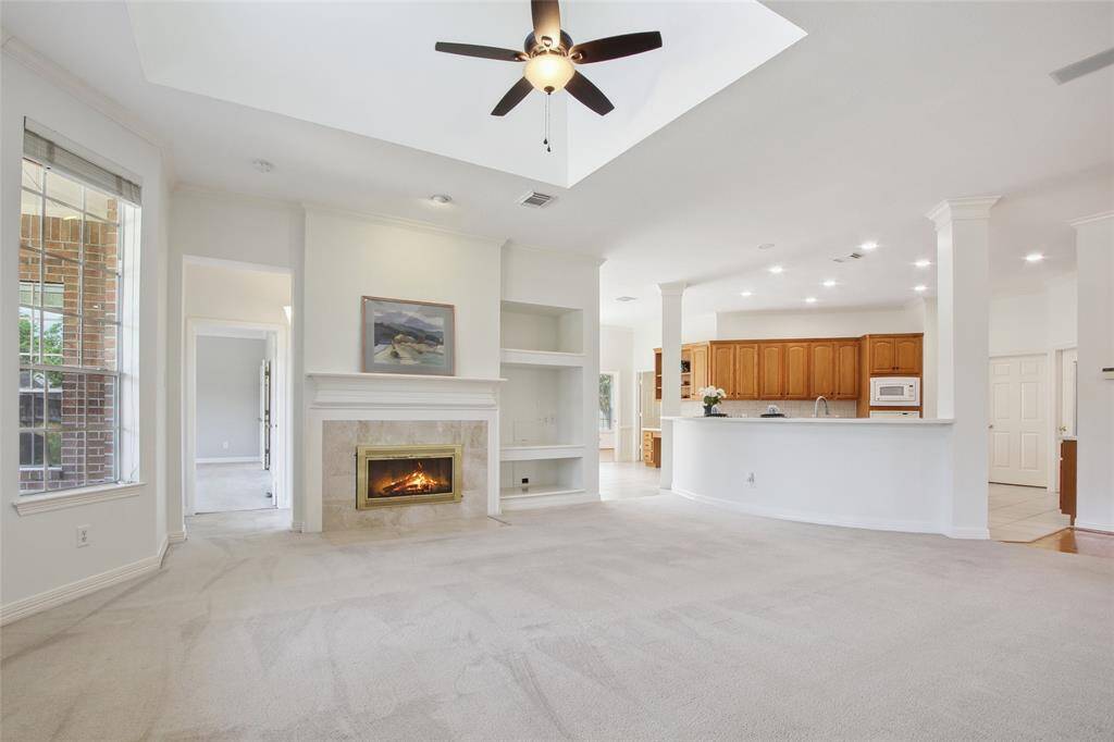 This spacious Family room features large windows for ample natural light, a cozy fireplace, built-in shelves, and a ceiling fan. The neutral color palette and open layout create a welcoming atmosphere, ideal for relaxation and entertaining.