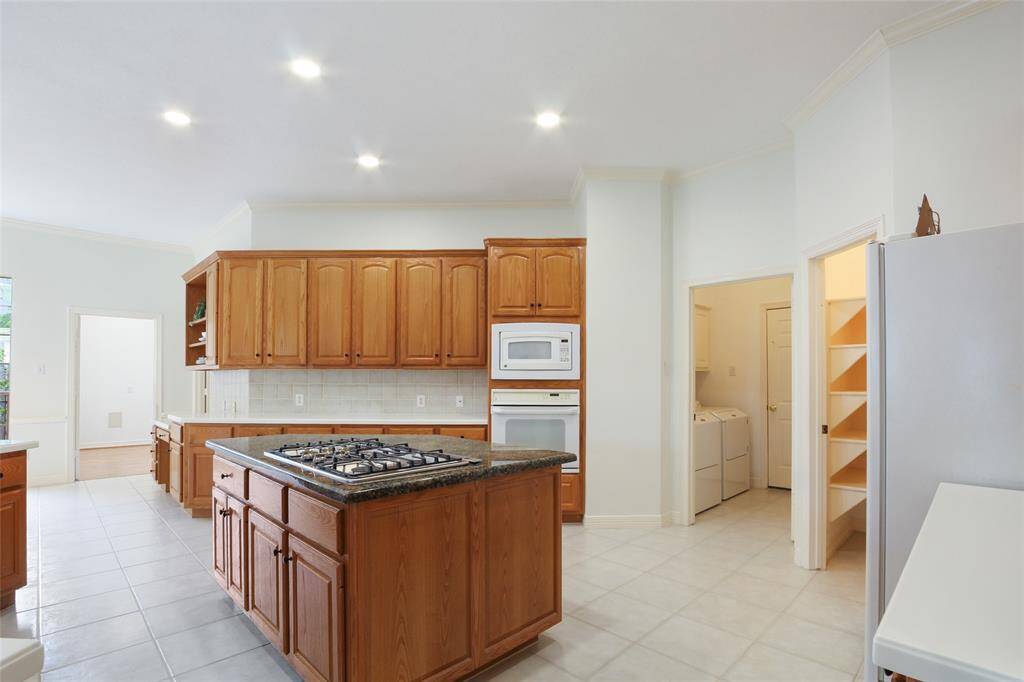 Spacious kitchen featuring wooden cabinets, a central island with a gas stove, and modern never used appliances. It has a sleek Large Farm sink and plenty of natural light, ideal for cooking and entertaining.
