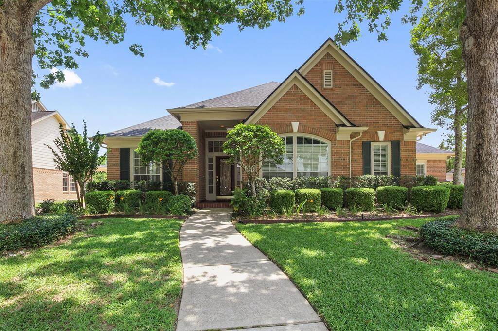 Charming brick home with a welcoming front porch, well-maintained landscaping, and a walkway framed by lush greenery, offering great curb appeal in a serene neighborhood setting.