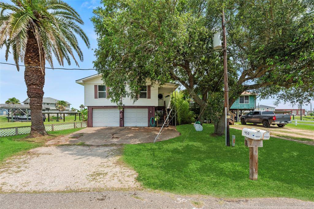 Elevated coastal-style home shaded by mature trees with a double driveway, two-car garage, and inviting front porch entry.