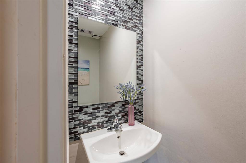 Downstairs half bath is guest-ready with a stylish tile accent wall and pedestal sink.