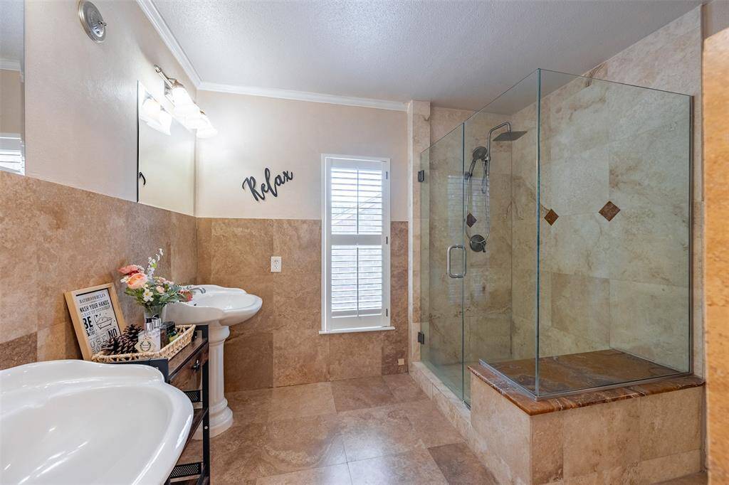The primary bathroom boasts double vanity, a glass walk-in shower with natural stone tile and a built-in bench.