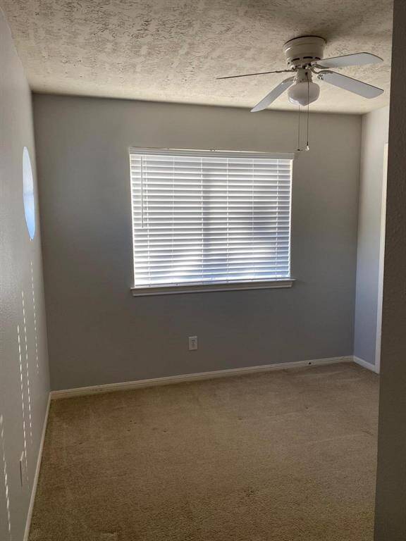 This room features neutral walls, a ceiling fan, and a window with blinds, providing natural light. It includes a closed door with a brass doorknob, suitable for a small bedroom or office space.
